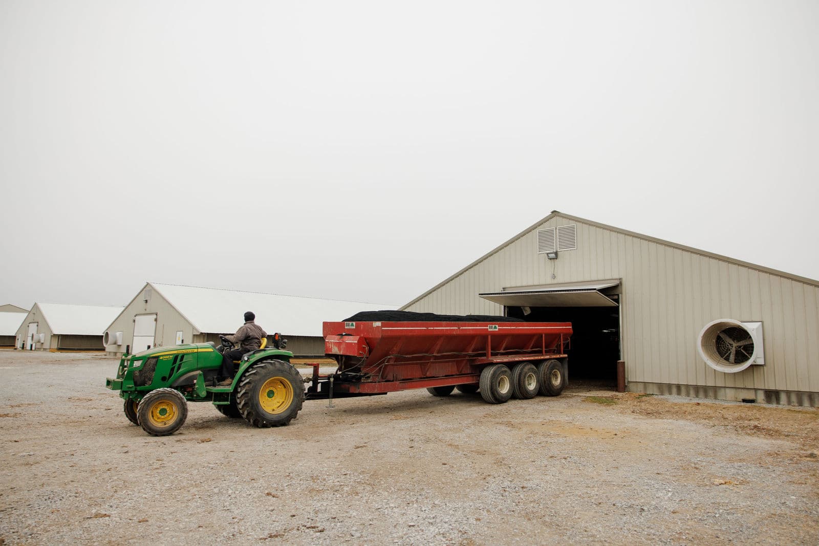 A tractor pulls an AeroChar spreader out of a poultry barn.