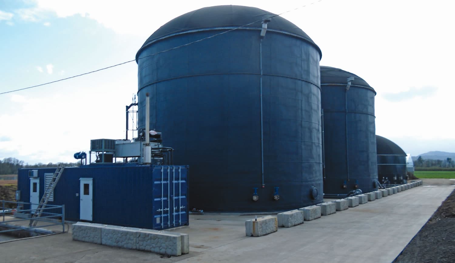 Two domed anaerobic digester tanks alongside a plant room at a farm-scale digester site.