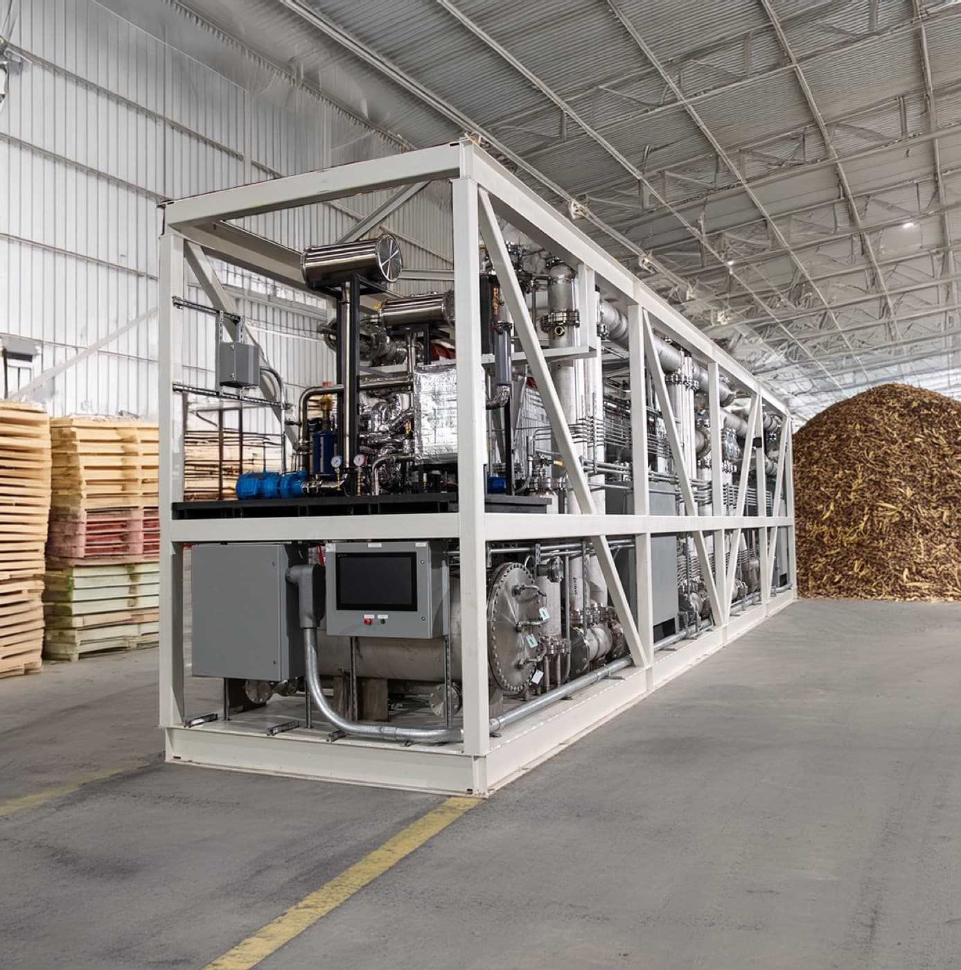 A LOCOAL Rainmaker unit in a framed skid inside the 48forty facility, wood residuals piled behind.