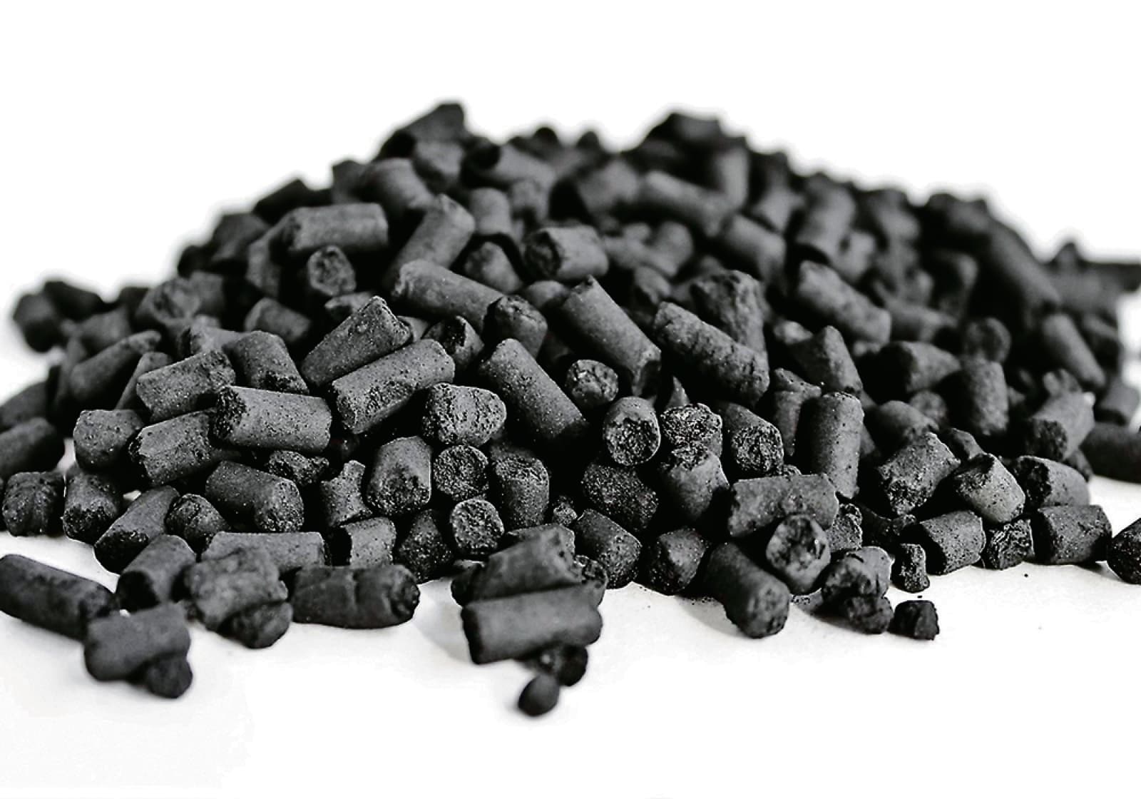 A heap of short cylindrical black biocarbon pellets on a white surface.