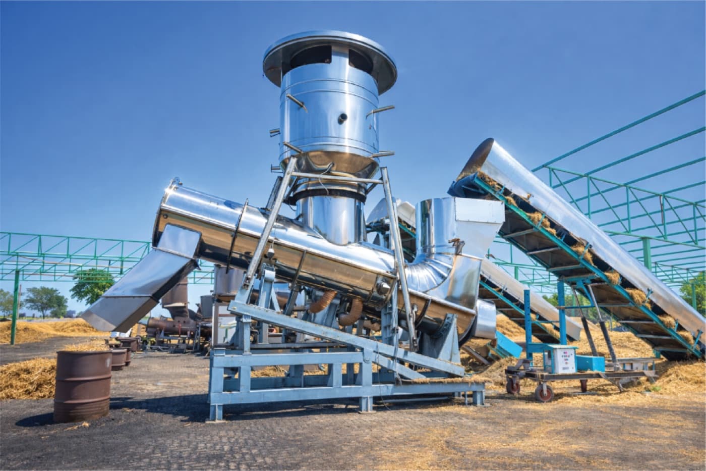 A polished stainless Takachar pyrolysis unit and conveyors on a straw-covered site.